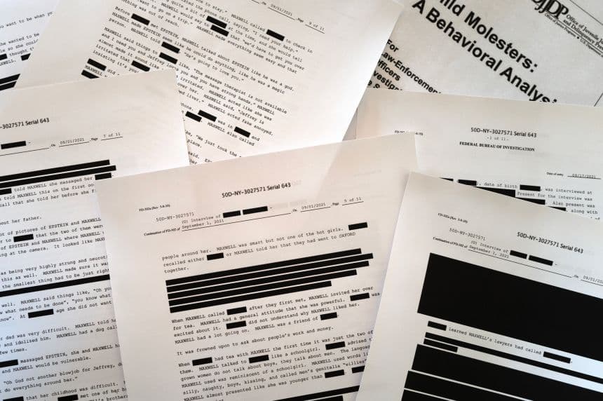 Heavily redacted pages from FBI interview files in the Jeffrey Epstein case spread across a table
